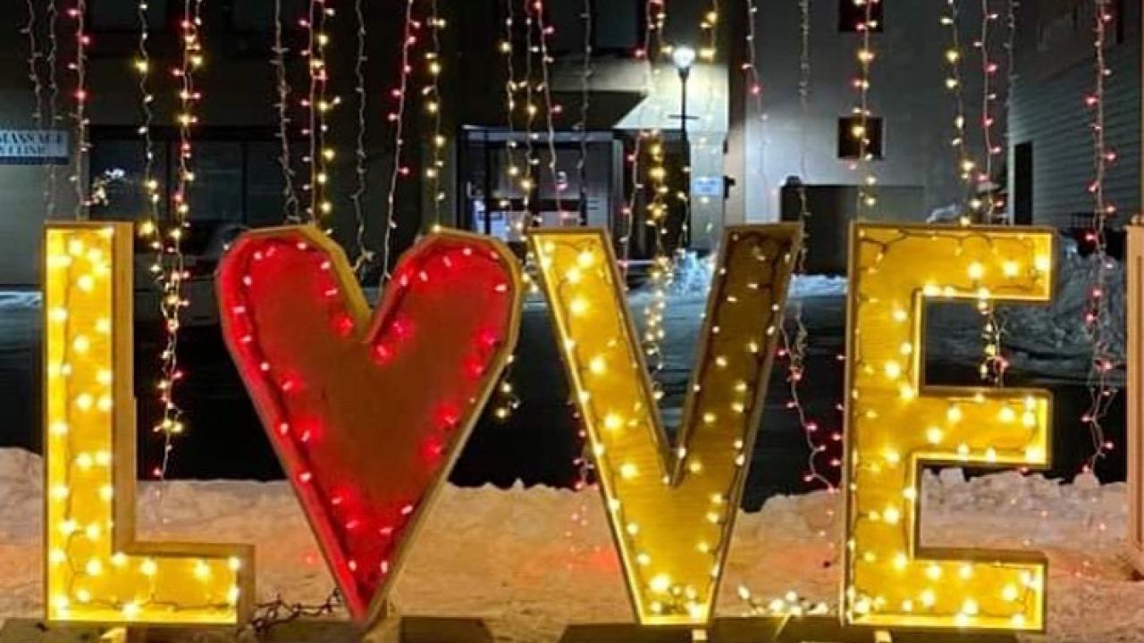 A glowing wooden sign that spealls "love" is illuminated by white lights against a backdrop of more hanging lights