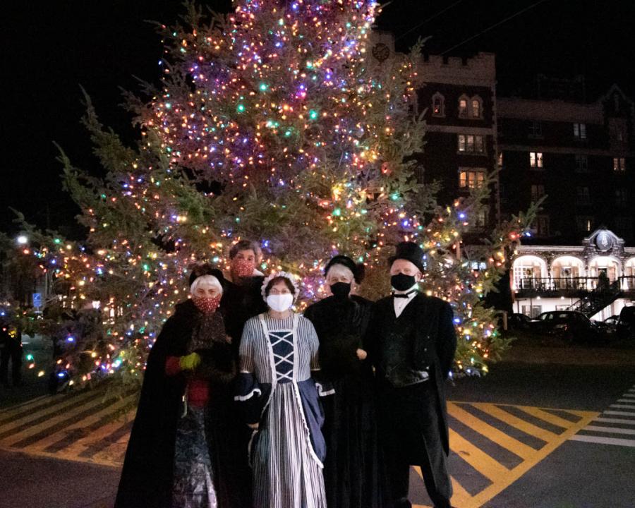 carollers are standing in front of a large colourfully lit chrsitmas tree in downtown kentville.  This image is from last year's holly days festival