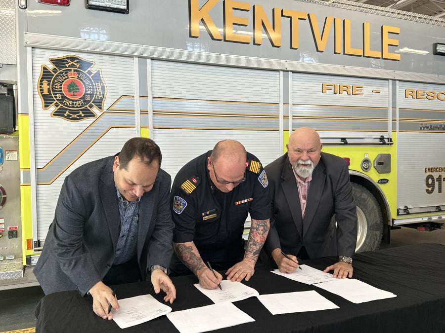 three men sign a paper with a firetruck visible in the background