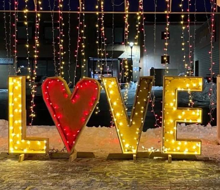 A glowing wooden sign that spealls "love" is illuminated by white lights against a backdrop of more hanging lights