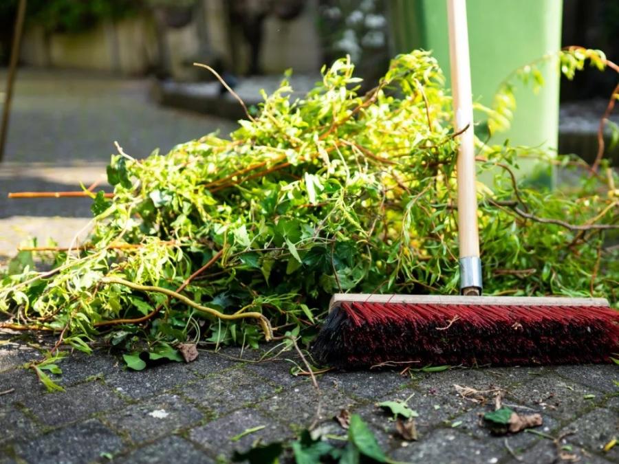 a broom sweeps ranches and leaves left behind from a serious rain storm.  The broom had red bristles and a white handle and is working on clearing a pathway made of cobbled stone. 
