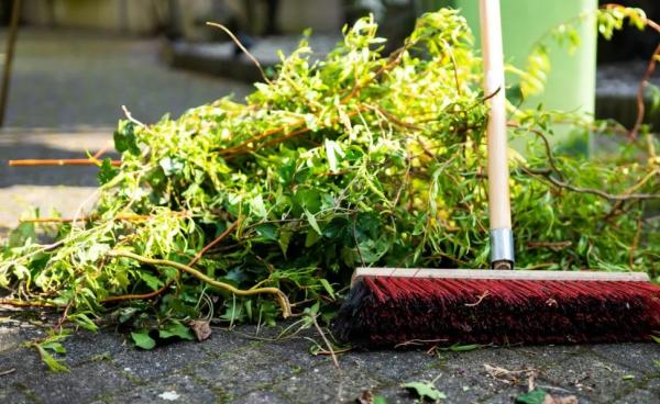 a broom sweeps ranches and leaves left behind from a serious rain storm.  The broom had red bristles and a white handle and is working on clearing a pathway made of cobbled stone. 
